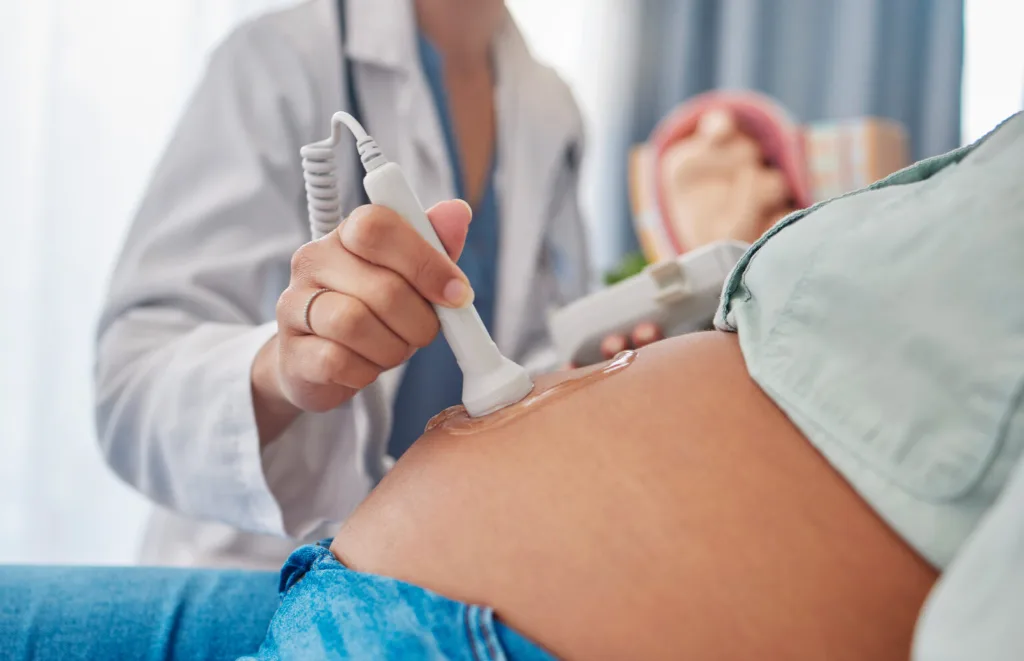 Sonde d'échographie posée sur le ventre d'une femme enceinte par une soignante